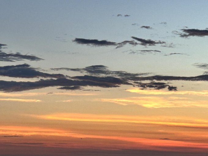 A serene sunset sky photograph featuring scattered dark clouds against a gradient of orange, pink, and blue colors.
