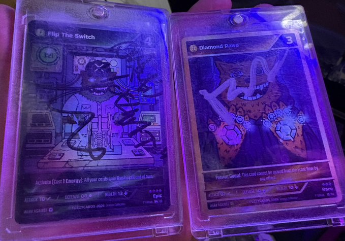 Two holographic Fuzzy Card collectible NFT trading cards displayed under purple UV light: a holographic-prism "Flip The Switch" Epic attack/defense card (Attack 10, Defence 10, Health 13, cost 4) on the left, and a Rare "Diamond Paws" card (Attack 0, Defense 10, Health 10, cost 3) on the right, illustrating the user's pride in collecting these digital cards rather than assigning them monetary value.
