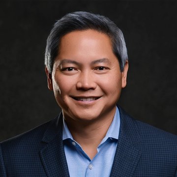 A smiling man with short dark hair wearing a blue shirt and dark checkered blazer, pictured in a professional headshot against a dark background. The image appears to illustrate Phong Le, the CEO of Strategy (formerly MicroStrategy), who is quoted discussing potential cryptocurrency and digital asset developments ahead.
