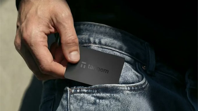 Close-up photo of a hand pulling a black 'Tandem' branded card from a denim jeans pocket.