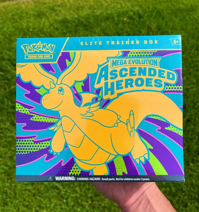 A person holding a 'Pokémon Trading Card Game: Elite Trainer Box' featuring the 'Mega Evolution Ascended Heroes' set, showing Dragonite artwork in vibrant blue, purple, and green colors.