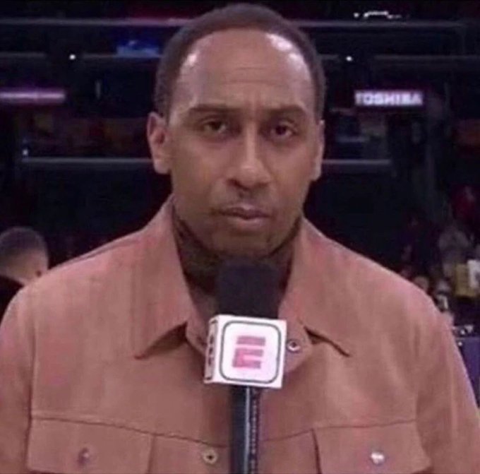 A close-up of sports commentator Stephen A. Smith holding an ESPN microphone while wearing a tan leather jacket.