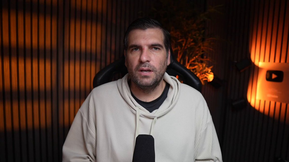 The image features a man wearing a white hoodie, sitting in front of a wall with orange lights behind him. The man appears to be making a funny or serious face as he looks directly at the camera. The background includes a plant, which adds an interesting element to the scene. The post that accompanies this image is titled "Stop ignoring Cardano. It just fixed scaling Cardano just crushed the skeptic narrative with a live deployment that critics claimed was physically impossible". This suggests that the man in the image might be discussing or highlighting the impressive capabilities of Cardano, possibly as part of a humorous or satirical commentary on the hype surrounding the cryptocurrency.