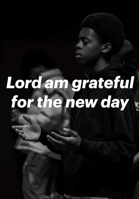 A black and white photo of a young person with hands raised in prayer, overlaid with the text "Lord am grateful for the new day".