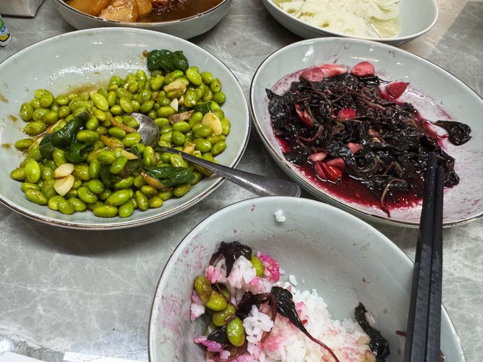 A homemade meal featuring edamame beans with garlic and peppers, a vibrant purple/red seaweed or wild vegetable dish, and a bowl of rice mixed with the same red vegetables, showcasing the daughter's appreciation for her mother's vegetarian cooking. The post humorously asks how many people have tried the distinctive red dish and can guess its name.