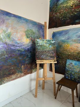 An art studio corner displaying several impressionist-style paintings of water lilies and landscapes, with a smaller canvas on a wooden easel.