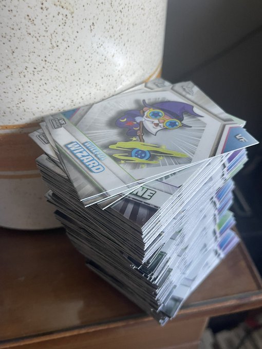 A stack of Pokemon cards sits on a wooden surface next to a speckled vase, with the top card showing an Articuno and a 'WIZARD' card visible.