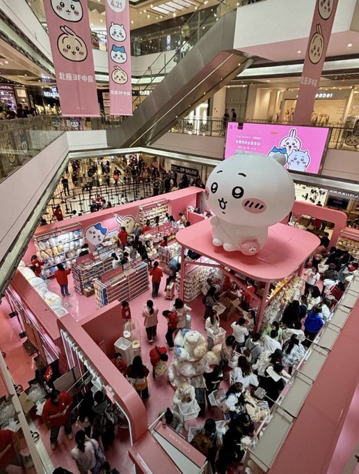A massive, crowded Chiikawa-themed pop-up event fills a multi-level shopping mall, featuring a giant inflatable mascot on a pink platform surrounded by merchandise displays and banners marked "4.21" — illustrating the viral IP's explosive popularity ahead of its movie release, and underscoring the post's bullish case for the $Chiikawa token.