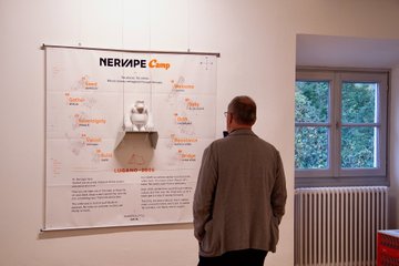 A man stands studying a wall chart titled “NERDPEA Company,” covered with small notes and a central diagram, beside a window and radiator.