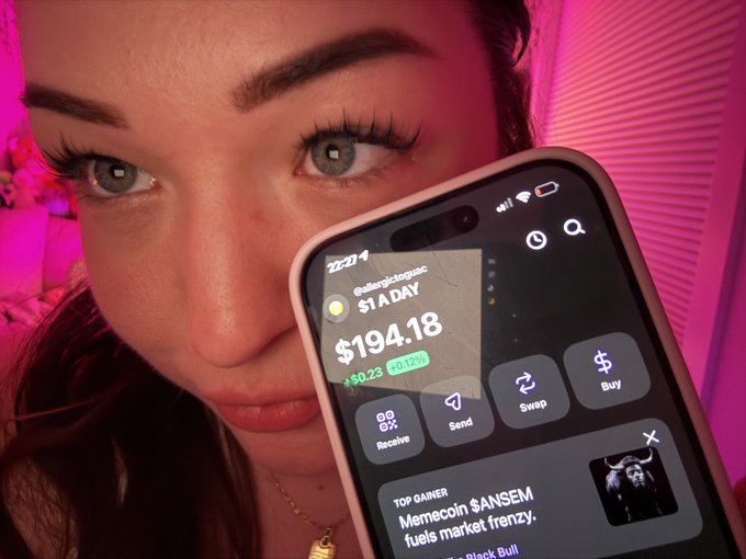 Close-up of a woman holding a smartphone displaying a crypto trading app showing a balance of $194.18 and '1 A DAY' growth, with the time reading 22:01.