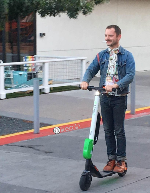 A man in a denim jacket rides a Lime e-scooter down a city sidewalk while smoking a cigarette, with a "L⚭tecoin" sticker visible on the ground nearby.