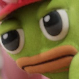 A close-up of a Pepe the Frog plush toy with large, glossy eyes and a pink hat, looking slightly off to the side.