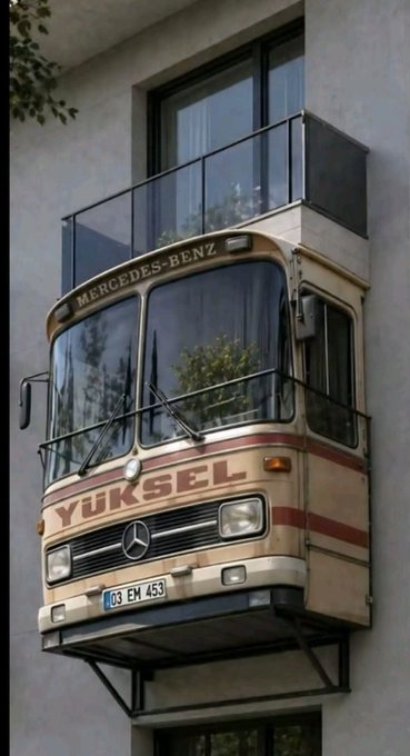 The front end of a vintage Mercedes-Benz bus, featuring a license plate reading '03 EM 453', has been creatively converted into a balcony on the side of a building. The word 'YÜKSEL' is painted in red letters across the front of the bus.