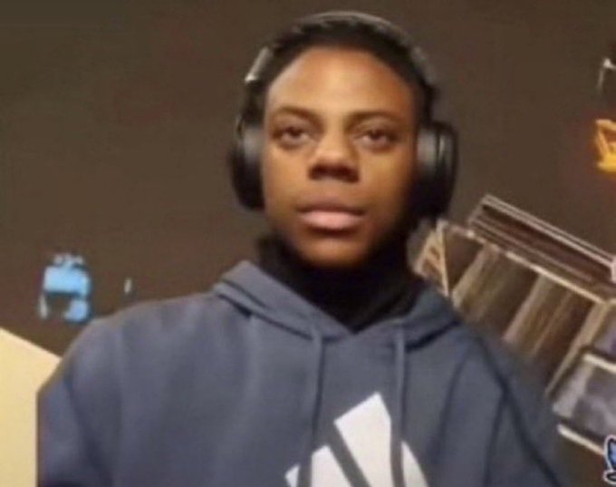 A young man wearing headphones and a dark hoodie sits in front of a computer in a dimly lit room.