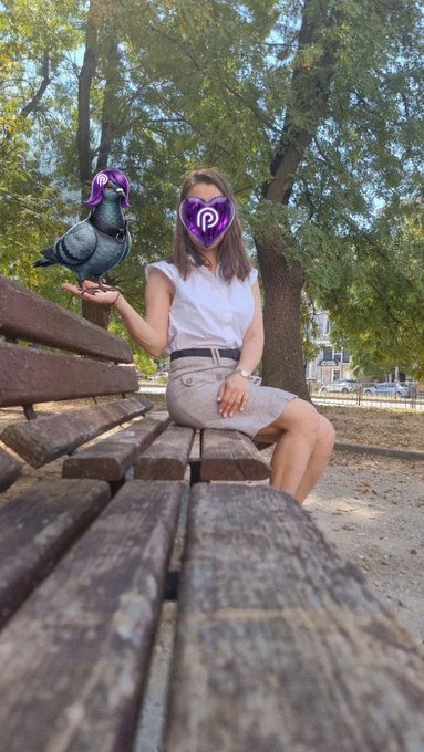 A woman in a white shirt and gray skirt sitting on a wooden park bench holding a pigeon, with a purple Pinterest logo covering her face.
