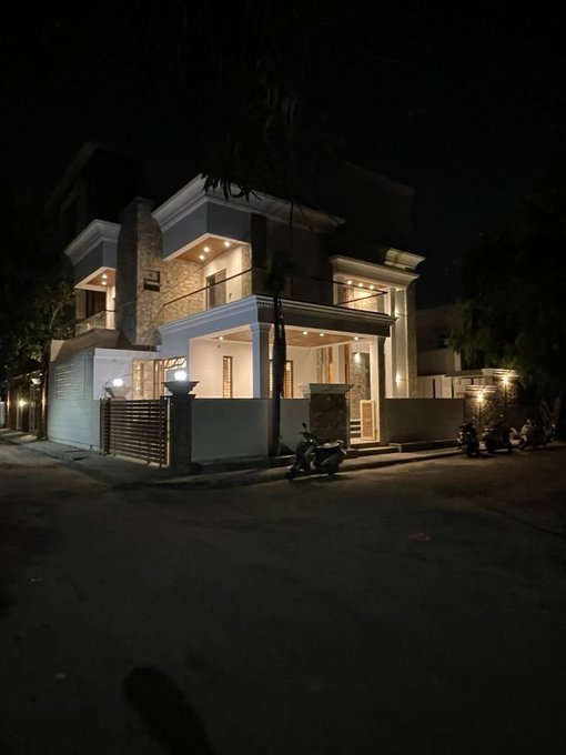 A modern, two-story house illuminated at night with warm exterior lighting stands at the end of a quiet street, with a motorbike parked out front. The image's calm, residential setting contrasts with the post's message about bringing intelligence closer to onchain activity, perhaps symbolizing decentralized infrastructure grounded in everyday environments.