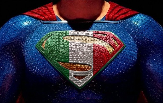 A close-up of Superman's chest emblem featuring the Italian flag colors instead of the traditional yellow and red, teasing a major announcement scheduled for Wednesday at 15:00 CET. The Italian-themed superhero imagery strongly suggests the upcoming reveal has significant relevance to Italy.