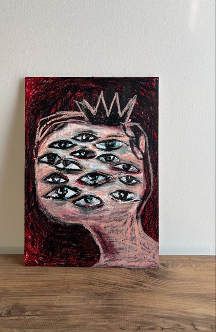 A painting on canvas leaning against a white wall, depicting a pink face covered in many eyes and wearing a small crown against a dark red background.