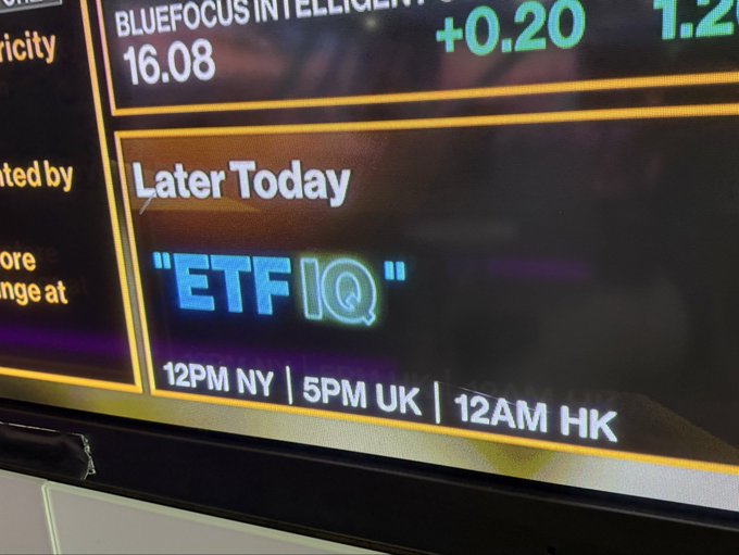 A close-up of a financial TV screen displaying a promo for "ETF IQ" airing later today at 12PM NY / 5PM UK / 12AM HK, with partial stock data showing "BLUEFOCUS INTELLIGENT" at 16.08 (+0.20) above it. The image relates to the post by setting the financial news backdrop against which Robbie Mitchnick discussed BlackRock's IBIT Bitcoin ETF and its reduced in-kind exchange minimum.