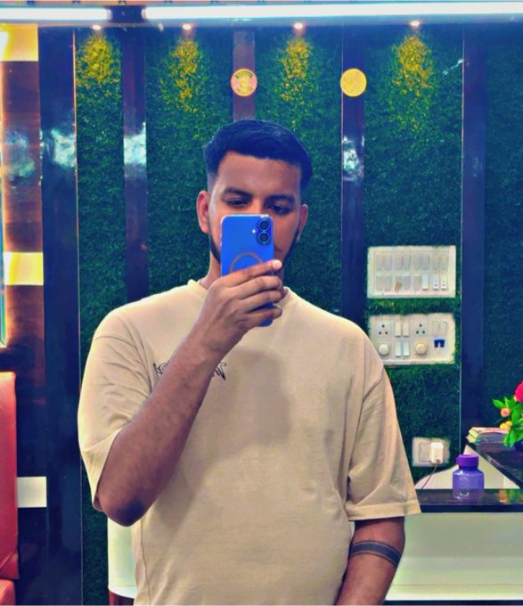 A man in a cream t-shirt takes a mirror selfie with a blue smartphone, standing in front of a green wall with electrical outlets, while the caption contrasts the stability of @quipnetwork with the weekly resets of @sleepagotchi.