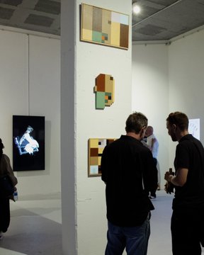 People viewing contemporary abstract artwork displayed on white walls and pillars in an art gallery.