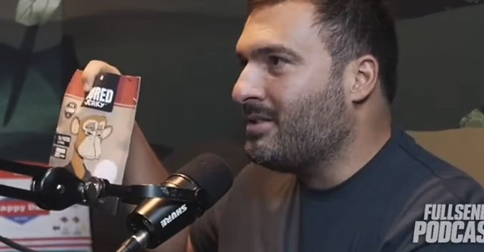 A bearded man in a dark shirt speaks into a Shure microphone while holding up a package of "Bored Jerky" featuring a cartoon ape character, with a "FULL SEND PODCAST" logo visible in the corner, appearing to discuss the product during an episode.