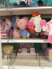 A shelf display of plush toys featuring Hello Kitty dressed in a pink kimono alongside other character plushies, with a small price tag visible.