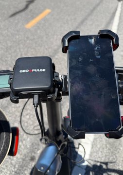 A "GEO-PULSE" device and a smartphone are mounted on a bicycle's handlebars, ready for outdoor GPS tracking. The setup demonstrates the transition from theoretical precision to real-world application, as suggested by the post.