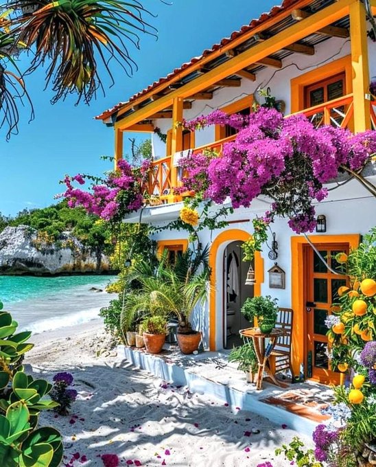 A vibrant coastal scene showing a white and orange house with bougainvillea flowers on its balcony, overlooking a turquoise sea.