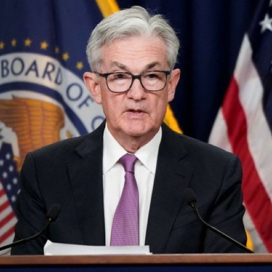 Federal Reserve Chairman Jerome Powell speaking at a podium, with the Federal Reserve seal and American flag visible in the background.