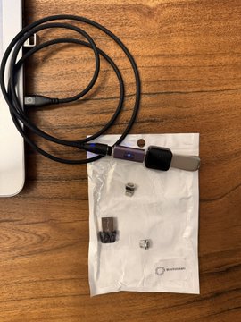 A coiled USB-C cable and a small white pouch containing adapter tips are laid out on a wooden surface, with the Blockstream Jade hardware wallet tag visible at the top. The post suggests these items may be accessories shipped with a Blockstream Jade device, prompting the user to question whether the cable is genuinely from Blockstream or an unverified adapter that accidentally entered the supply chain.
