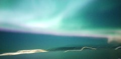 A blurry vertical image showing streaks of teal and green light, possibly an aurora or long-exposure night photography, with indistinct bright shapes at the bottom.