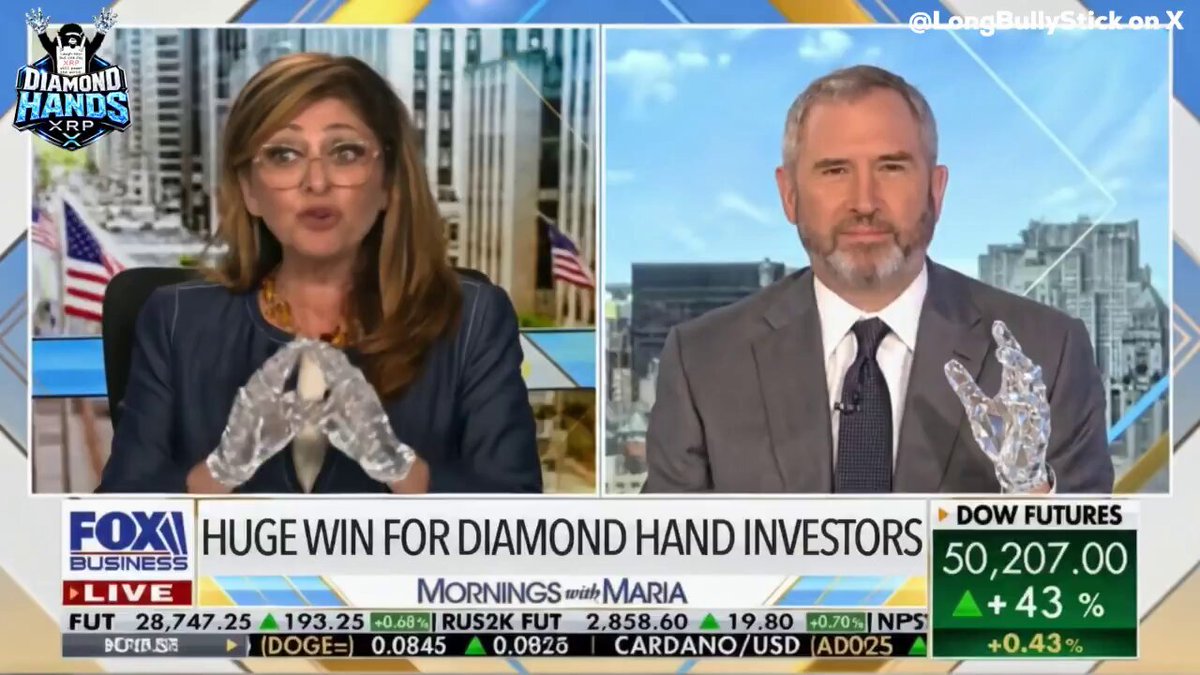 The image features a news segment with two people, a man and a woman, sitting at a desk and talking about diamonds. The woman appears to be wearing glasses while they discuss the topic. They are seated behind a desk that has an American flag on it, suggesting that this might be a newsroom or a studio setting. The image also includes text related to Bitcoin and diamonds, which could indicate that the conversation is taking place in relation to these topics.