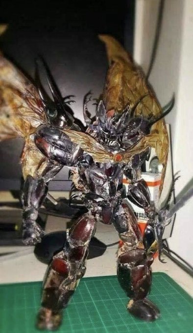A detailed action figure or sculpture of a dark, winged insectoid warrior stands on a green cutting mat.