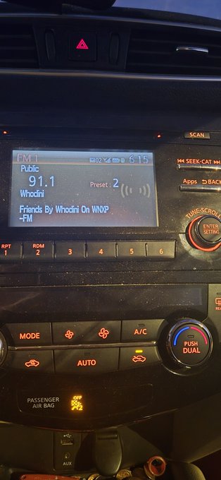 A car dashboard radio display shows it's tuned to 91.1 FM 'Whodini' playing 'Friends By Whodini On WNXP-FM', with climate controls visible below.