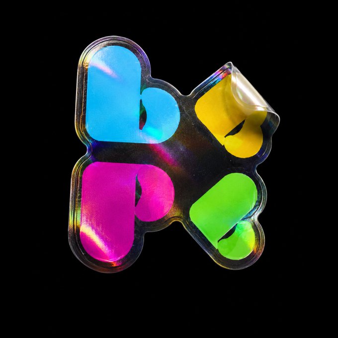 A colorful, holographic dog bone-shaped sticker against a black background, displaying "BP" in vibrant blue, magenta, yellow, and green letters, connecting visually to the "GM Beepers" reference.