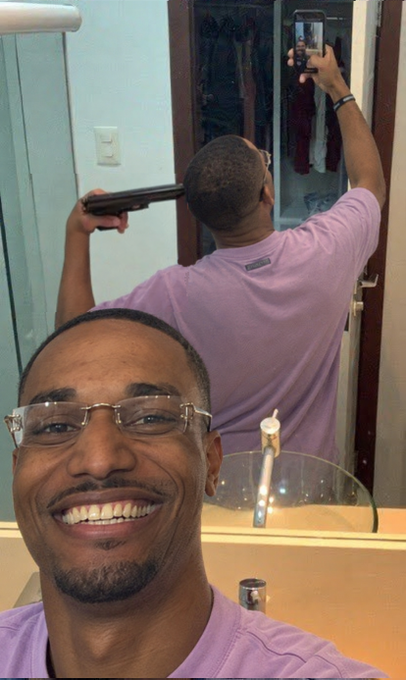 A smiling man with glasses takes a mirror selfie in a bathroom while holding a hair straightener behind his head, cleverly referencing the Chicago Bulls logo by mimicking its charging bull silhouette with his playful pose.