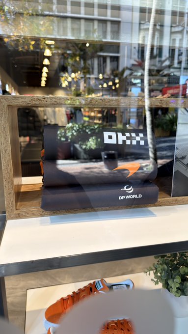 A display case shows merchandise branded with the "DP World" logo, including a folded item and an orange strap. Echoing the caption "Chance encounters anytime, anywhere," the DP World branded items are showcased in what appears to be a public-facing space like a store window or atrium, suggesting that unexpected connections with the brand can happen in everyday settings.