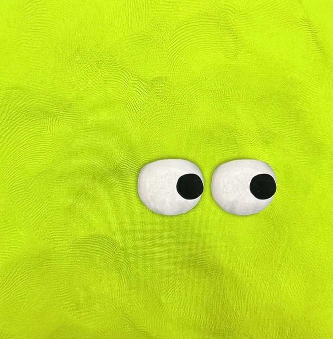 Two cartoonish googly eyes are placed on a textured lime-green fabric background.