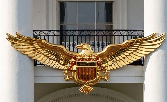 A gilded eagle emblem with outstretched wings, encircled by stars, is mounted on the white facade of a building above a black wrought-iron balcony. The majestic, soaring eagle visually echoes the post's metaphor of XRP "flying high like on eagle's wings," symbolizing upward momentum and ambition.
