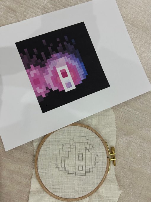 A printed pixel art NFT featuring a pink and purple "zk" design sits above a wooden embroidery hoop containing the work-in-progress cross-stitch version, showing the central "zk" letters outlined in pencil on cream fabric. The image illustrates the creative process of translating a digital zkSNARKs NFT into a handcrafted textile piece.