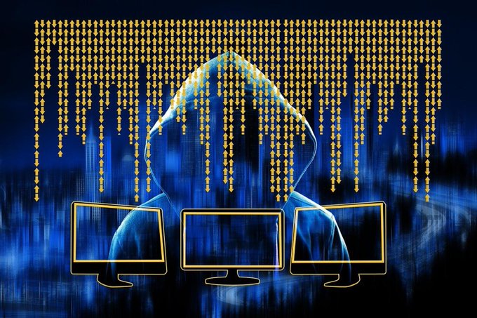 A hooded figure looms over three computer monitors as streams of yellow arrows rain down, symbolizing a data breach or cyber attack.