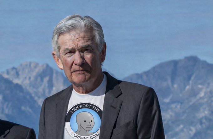 A serious-looking older man with gray hair stands against a mountainous backdrop, wearing a t-shirt that reads "I SUPPORT THE CURRENT CONSPIRACY" featuring a cartoon alien head. The image playfully connects to the post's mention of "$NPC" (Narrative Protocol Coin or similar meme token), as "NPC" refers to "non-player character"—a fitting visual pun for a conspiracy-themed shirt and the meme coin hype.