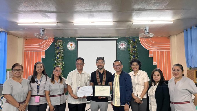 A group of nine people posing together in what appears to be a school or institutional setting, with two individuals in the center holding certificates of appreciation.