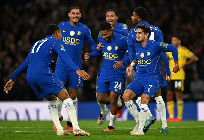 Chelsea players in their blue kits, featuring the "USDC" sponsor logo on the front, celebrate a goal with player #24 Reece James prominently visible, embodying the "boys in blue" theme of the post.