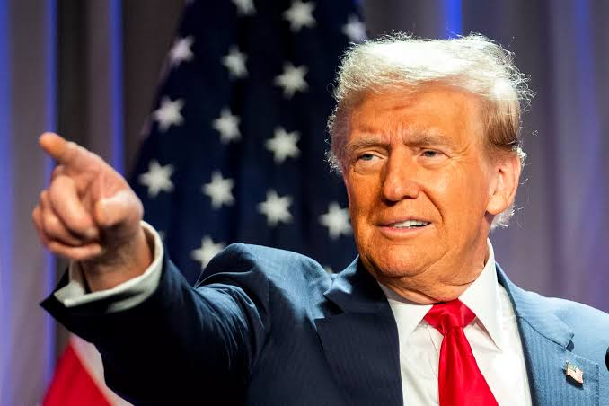 Donald Trump is pictured pointing forward in front of an American flag. This image may be used to represent a political figure's endorsement or support of the Clarity Act and financial innovation.