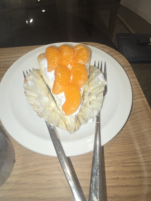 The image features a white plate with a dessert, which appears to be a piece of cake or pie topped with orange slices. The plate has two forks placed on top of it, suggesting that someone is about to enjoy this treat. The background shows a wooden table and a glass, indicating that the setting might be indoors. The post in question seems to be discussing the dessert's presentation, possibly highlighting its visual appeal or sharing a recipe for similar dishes.