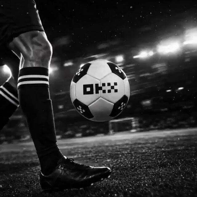 The image features a soccer player kicking a white soccer ball with black lettering, which has the letters "OKX" written on it. The scene takes place at night during a nighttime soccer game or practice session.