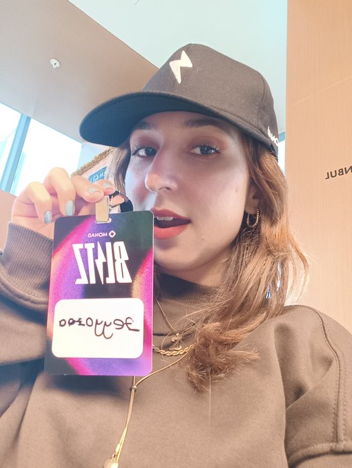 A young woman wearing a black cap and beige sweater holds up an "BRTS" branded badge with "gmonad" handwritten on it, posing for a selfie in what appears to be a corporate setting with "NAUTIL" visible in the background.

The image ties to the post by showcasing her "gmonad" ID badge, visually identifying her as part of the Monad community referenced in the tagged accounts.
