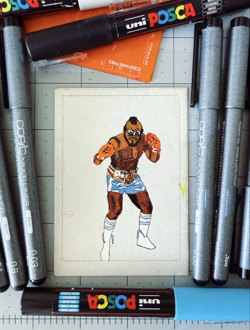 A small hand-drawn illustration of a masked wrestler in blue trunks is surrounded by Copic Multiliner pens and Uni Posca markers on a desk.